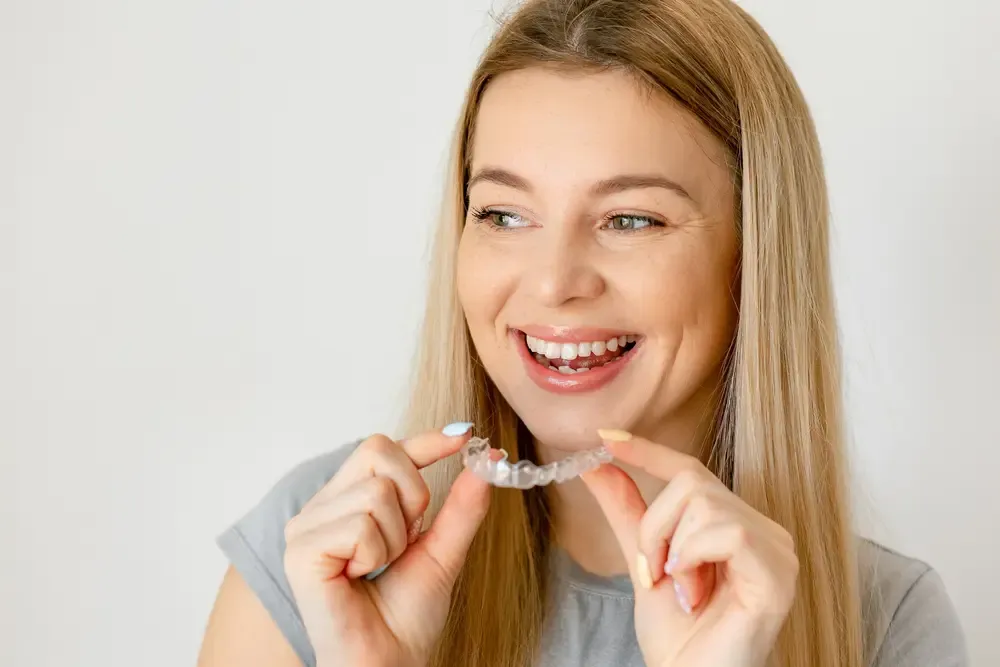 Woman smiling as she holds a clear aligner